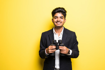 An Indian businessman in his late thirties looking through binoculars isolated on yellow background