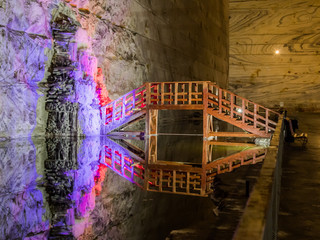 Illuminated stalactites from salt and wooden bridge across the reservoir in salt mines in Slanic -...