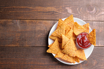 Chips. Nachos on a white plate with red sauce on a brown wooden background with a place for an inscription. View from above