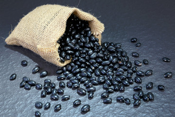 Close-up photo uncooked Vigna mungo or Black gram in sack on black table background. Foods and...