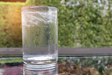 Cool drinking water in glass with ice inside on glass table with dry flower below, as natural in the morning with sunrise background. Drink concept.