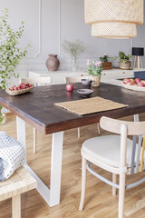 Real photo of a simple dining table, chair, flowers and lamp in a dining room interior