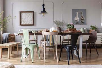 Real photo of an eclectic dining room interior with various chairs at the table, lamp and painting...