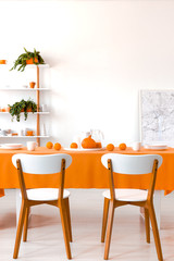 Plants and poster in white dining room interior with wooden chairs at table with orange cloth. Real photo