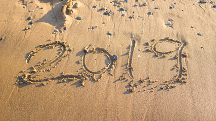 2019 - the date of the new year is written on the yellow sand by the sea or ocean. The concept of the New Year holidays and the onset of the new year twenty nineteen. Background
