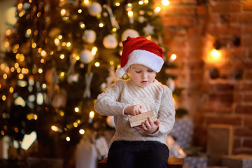 Cute little boy wearing Santa hat opening a Christmas gift