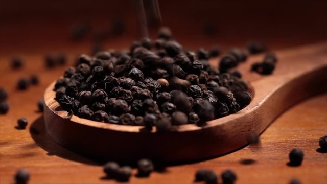 Black Tellicherry peppercorns closeup in wooden spoon on a kitchen table.