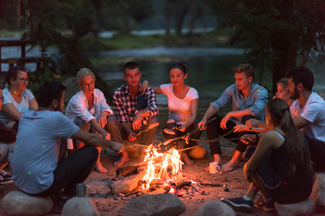young friends relaxing around campfire - Powered by Adobe