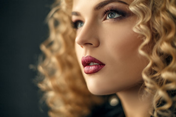 Closeup Beauty portrait of sexy curled hair blonde girl in studio with dark background