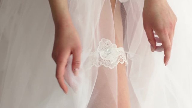 Close-up of a girl's leg with a garter for stockings. Sexy girl in transparent fluffy negligee and panties with stockings and garter, close-up.