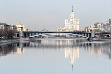 The city landscape overlooking the high-rise building and the bridge over the river is reflected in the calm water of the river.