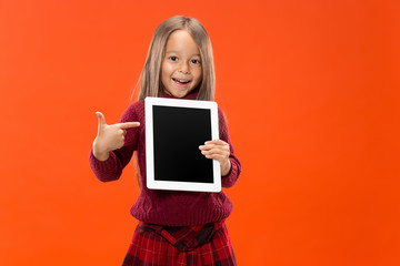 Little funny girl with tablet on studio background. She showing something and pointing at screen.