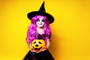 Small girl in Halloween witch dress and hat scaring and making faces isolated on yellow background....