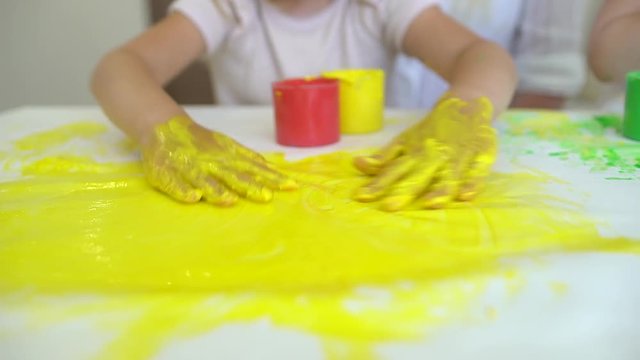 Happy family paints colors. Close up of happy little cute child's hands making paint colorful drawings on paper. A little cute happy funny girls painting color. Slow motion