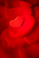 Small red heart on rose flower petals. Romantic background texture for a Valentine's or Wedding day greetings card with copy space.