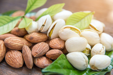 close up of almonds grain roast and Pistachios nuts on wood background with green leaves