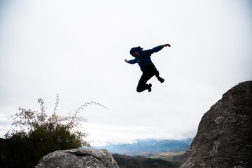 From below view of sportive man jumping from rock to rock doing parkour in afternoon.