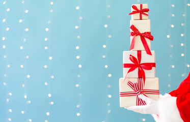 Santa holding Christmas gift boxes on a shiny light blue background