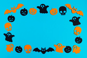 Frame from black and orange paper ghosts, pumpkins and skulls on a blue background. Holiday decorations for Halloween with copy space.