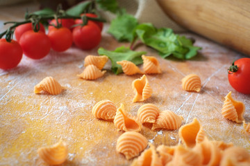 homemade conchiglie raw pasta with tomatoes on a wooden table with flour