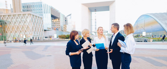 Beautiful businesswomen keeping blue document case talking with cheerful male boss outside. Concept...
