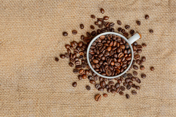 Fragrant Coffee Beans are poured into a white mug on a canvas. Panorama. Vintage background