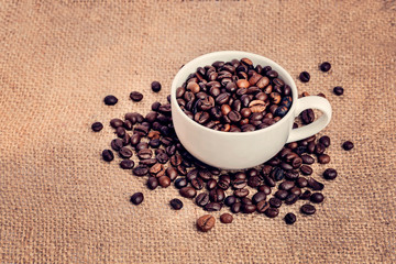 Fragrant Coffee Beans are poured into a white mug on a canvas. Panorama. Vintage background