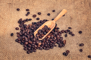Fragrant Coffee Beans are piled on a canvas with a wooden spoon on top. Vintage background.