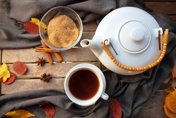 Obraz na płótnie Canvas tea cup and a white teapot on a wooden table with spices and some autumn leaves, high angle view from above, selected focus