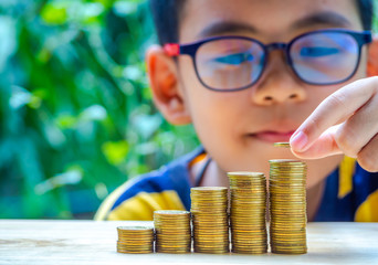 The Asian boy are stacking with coins to save the money for the future. Concept for loan, property ladder, financial, mortgage, real estate investment, taxes and bonus.