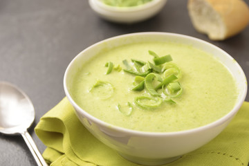 leek cream soup in a white bowl with napkin, spoon and bread on a dark table