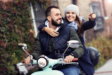 Beautiful young couple smiling while riding scooter in city in autumn © Kalim