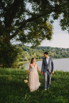 Wedding day. Beautiful handsome young couple on their wedding day standing in nature near river and looking at each other.