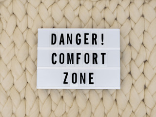  DANGER! COMFORT ZONE word on lightbox on knit background. COMFORT ZONE concept. 