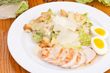 Caesar salad with grilled chicken breast, egg, parmesan cheese on white plate. Close up