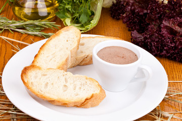 Chicken liver pate in cup and sliced baguette on white plate. Close up