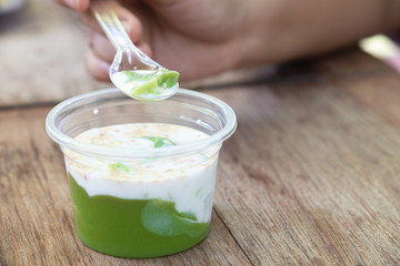 hand holding spoon and eating Khanom Peakpoon Thai sweet desert.