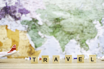 Travel text object and airplane toys on the wooden table, top copy space. World Map in background. Travel planning theme