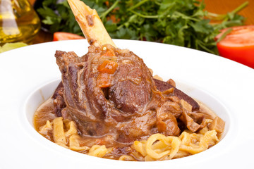 Lamb Osso Bucco with pasta and vegetables on white plate. Close up