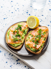 Rye bread avocado toasts with smoked salmon on white wooden board