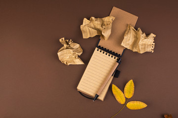 An open notebook for records and crumpled sheets on a brown background. Office planning. Free space for text. Autumn atmosphere and yellow leaves. Top view. Flat lay. Copy space.