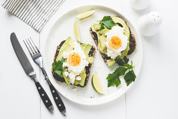 Avocado and egg on whole grain toast on white plate. Table top view, toned image