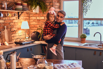 Cute little girl in rabbit makeup and hat sitting on hands of his father in loft style kitchen at morning.