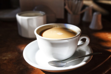 white cup with coffee in the morning rays of the sun