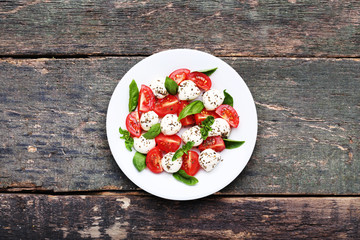 Mozzarella, tomatoes and basil leafs in plate on wooden table