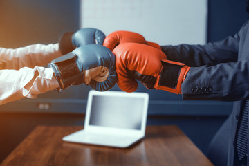 Man and woman in boxing gloves standing at table. Laptop on table. Fight of genders concept.