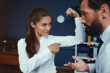 Young business woman showing muscles to her male colleague in office. Fight of genders concept.