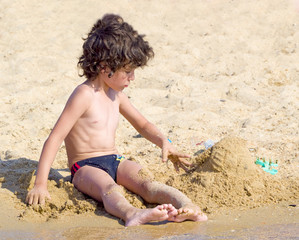 little boy building sand castle on beach
