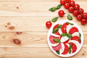 Mozzarella, tomatoes and basil leafs on brown wooden table