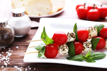 Sticks with mozzarella, tomatoes and basil leafs on wooden table